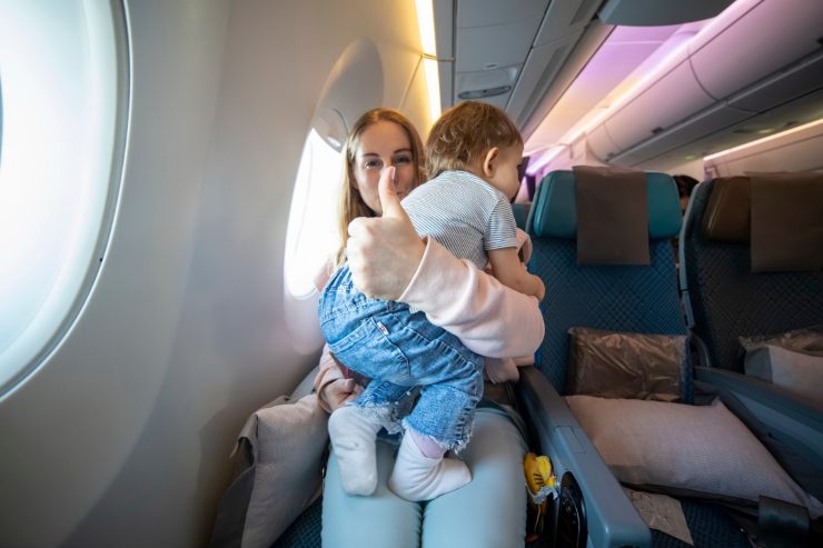 mamma in aereo che tiene in braccio un bambino piccolo e fa il segno "ok" con il dito