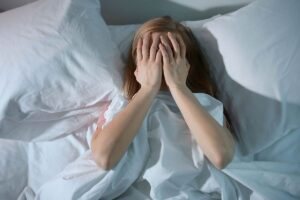Donna con mani sul viso nel letto