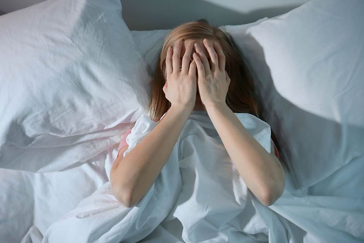 Donna con mani sul viso nel letto